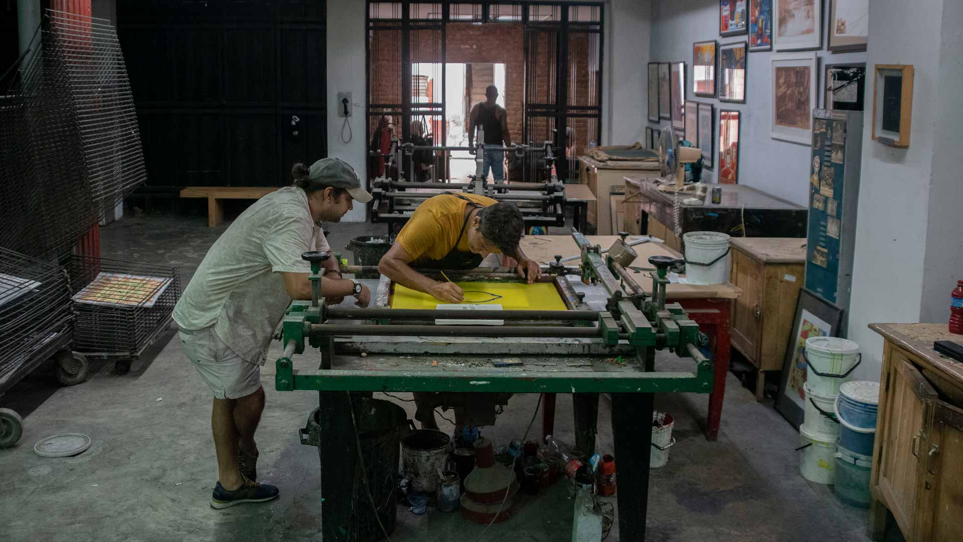 Two people working on a large printing press in a workshop setting.
