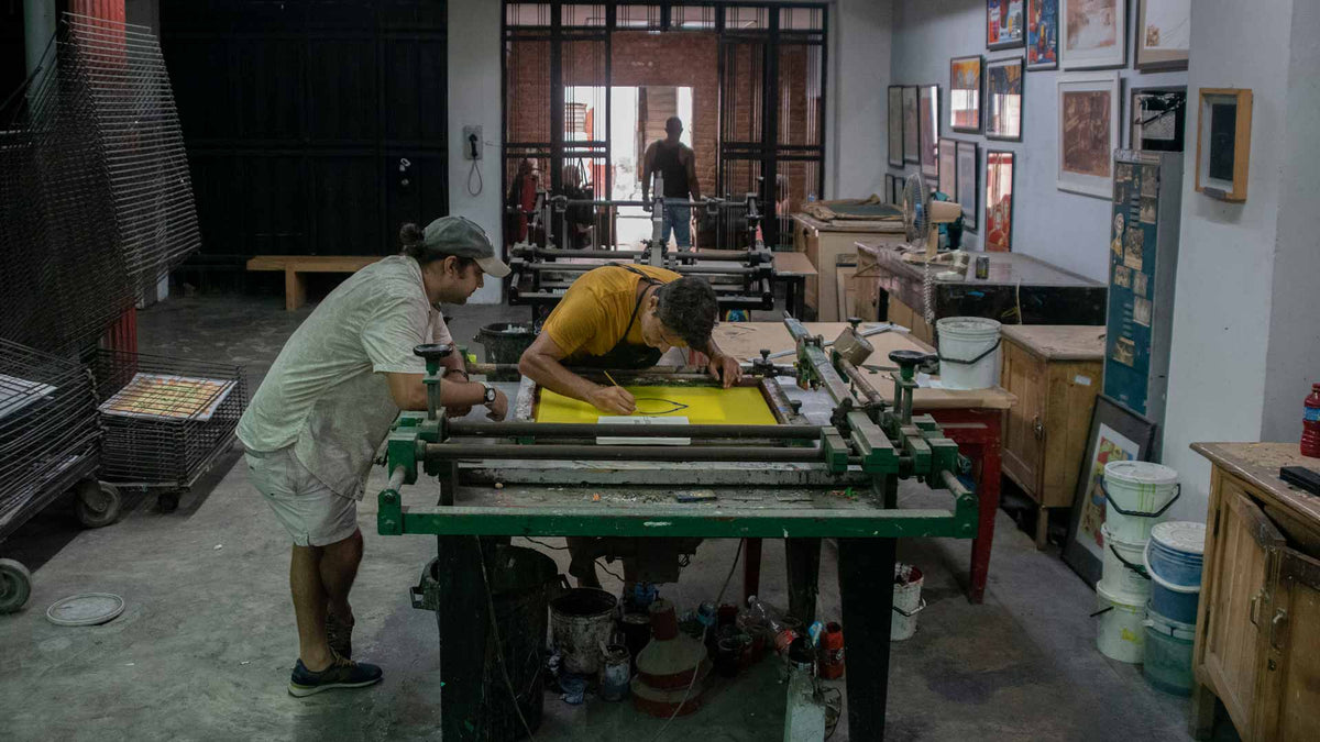 Two people working on a large printing press in a workshop setting.